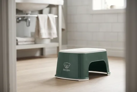 Deep green and white BabyBjörn step stool on a bathroom floor near the sink