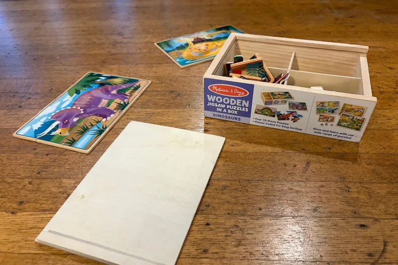 Our Melissa & Doug four-puzzle dinosaur set, with completed puzzles and divided wooden storage box on a table
