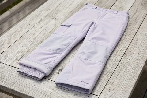 Lavender Columbia Kids Bugaboo III snow pants laid on a weathered wooden table