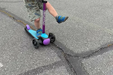 Child riding a purple and blue GOMO three-wheel scooter on dry pavement
