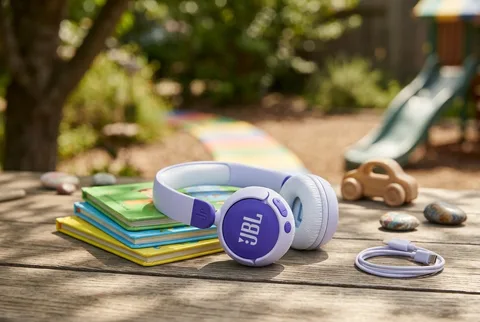 Purple JBL Junior 320BT headphones resting on a stack of picture books on an outdoor wooden table