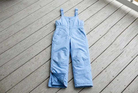 Light blue L.L.Bean Kids’ Cold Buster snow bibs laid flat on pale wooden floorboards