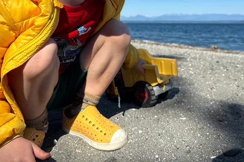 Yellow Native Jefferson shoes worn with socks on a rocky beach