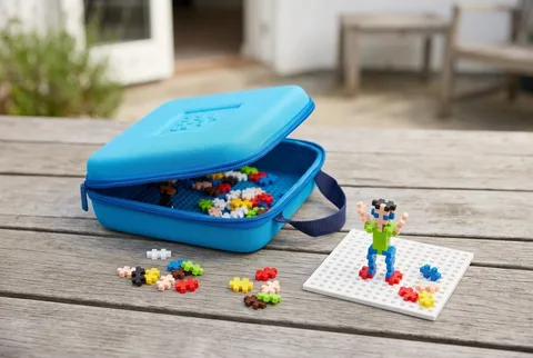 Blue Plus-Plus travel case with interlocking pieces and a small built figure on a wooden table