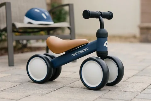 Navy Retrospec Cricket four-wheeled ride-on on a paved patio, helmet on a bench behind