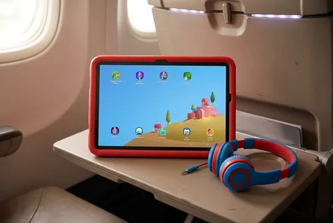 Samsung Galaxy Tab A11+ Kids Edition in a red bumper case on an airplane tray table beside kids headphones