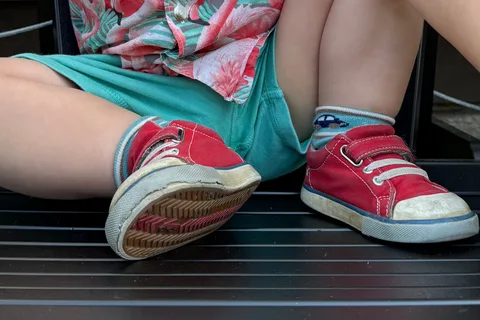 Red See Kai Run Stevie II shoes worn while sitting outdoors