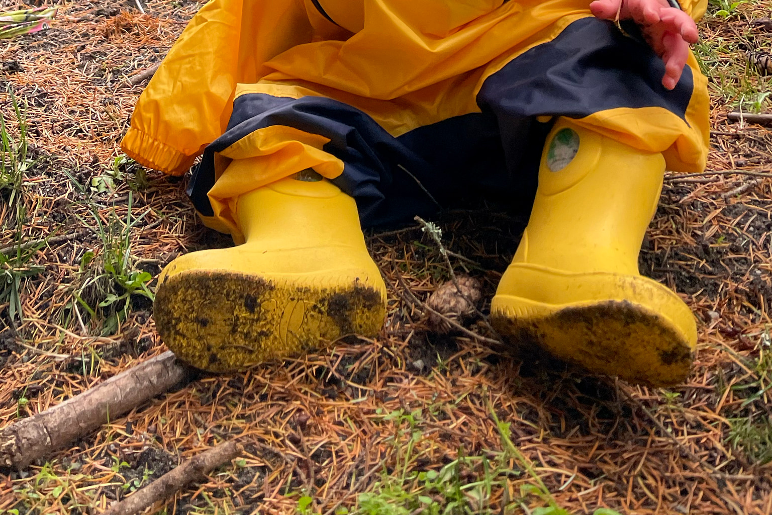 Mud-covered yellow Okabashi Kendall rain boots worn with rain pants outdoors